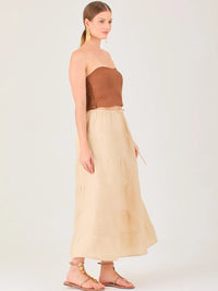 La falda es de largo midi, confeccionada en una tela ligera de tono beige claro. Presenta un diseño de corte amplio con caída fluida y detalles de costuras horizontales que crean un efecto de franjas sutiles a lo largo de la prenda. La pretina es elástica con cordón ajustable al frente, lo que le aporta comodidad y un estilo relajado. Su diseño minimalista y neutral la hace versátil, ideal para combinar con diferentes tops y accesorios, manteniendo un aire fresco y natural.
