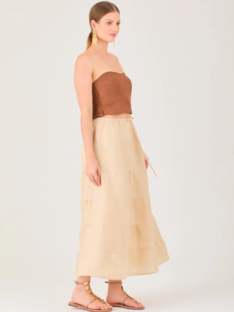 La falda es de largo midi, confeccionada en una tela ligera de tono beige claro. Presenta un diseño de corte amplio con caída fluida y detalles de costuras horizontales que crean un efecto de franjas sutiles a lo largo de la prenda. La pretina es elástica con cordón ajustable al frente, lo que le aporta comodidad y un estilo relajado. Su diseño minimalista y neutral la hace versátil, ideal para combinar con diferentes tops y accesorios, manteniendo un aire fresco y natural.