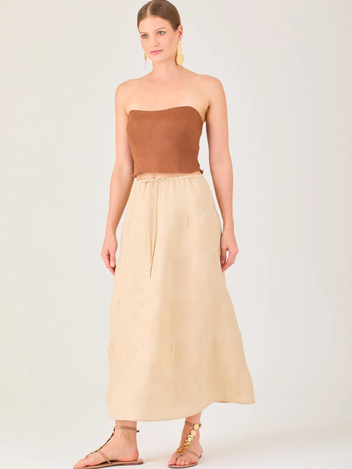 La falda es de largo midi, confeccionada en una tela ligera de tono beige claro. Presenta un diseño de corte amplio con caída fluida y detalles de costuras horizontales que crean un efecto de franjas sutiles a lo largo de la prenda. La pretina es elástica con cordón ajustable al frente, lo que le aporta comodidad y un estilo relajado. Su diseño minimalista y neutral la hace versátil, ideal para combinar con diferentes tops y accesorios, manteniendo un aire fresco y natural.