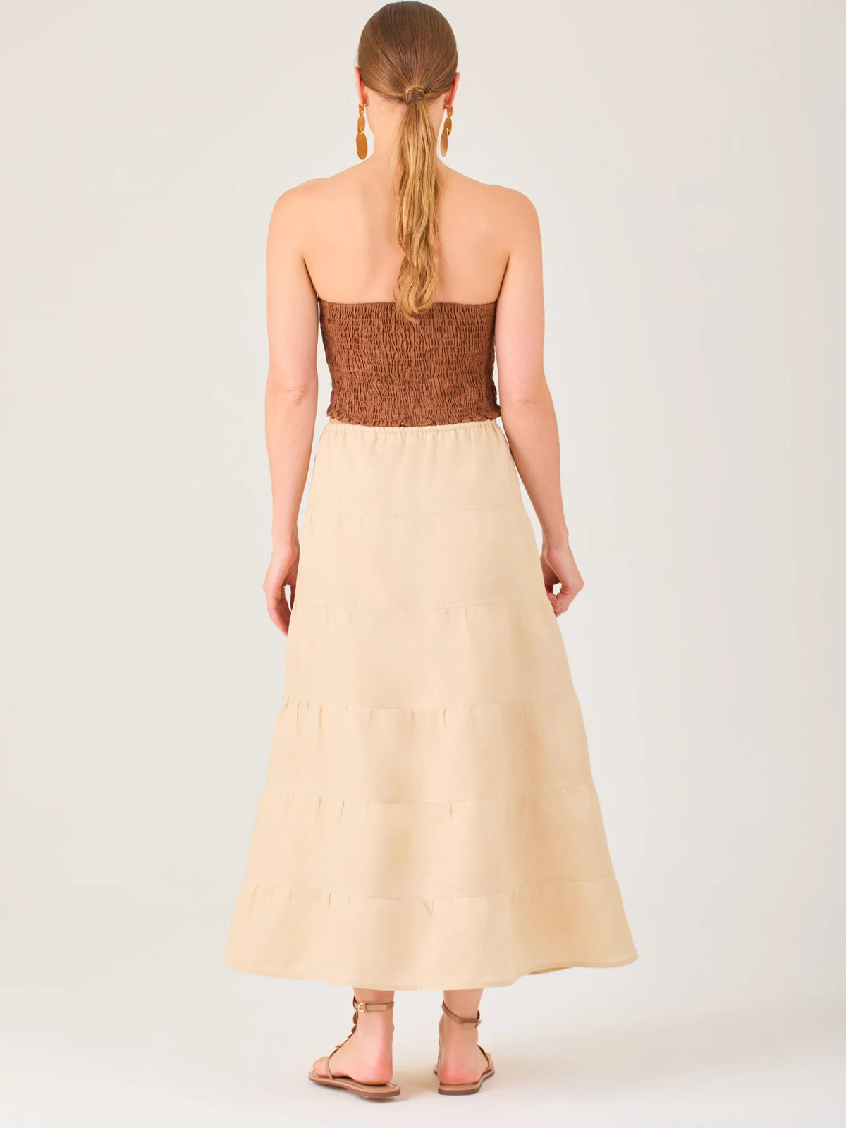 La falda es de largo midi, confeccionada en una tela ligera de tono beige claro. Presenta un diseño de corte amplio con caída fluida y detalles de costuras horizontales que crean un efecto de franjas sutiles a lo largo de la prenda. La pretina es elástica con cordón ajustable al frente, lo que le aporta comodidad y un estilo relajado. Su diseño minimalista y neutral la hace versátil, ideal para combinar con diferentes tops y accesorios, manteniendo un aire fresco y natural.