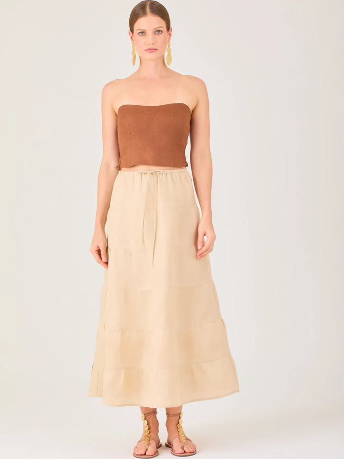 La falda es de largo midi, confeccionada en una tela ligera de tono beige claro. Presenta un diseño de corte amplio con caída fluida y detalles de costuras horizontales que crean un efecto de franjas sutiles a lo largo de la prenda. La pretina es elástica con cordón ajustable al frente, lo que le aporta comodidad y un estilo relajado. Su diseño minimalista y neutral la hace versátil, ideal para combinar con diferentes tops y accesorios, manteniendo un aire fresco y natural.