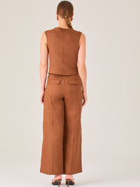 Este pantalón presenta un corte de pierna ancha y recta, confeccionado en una tela estructurada de tono marrón cálido. Tiene un diseño elegante y minimalista, con cintura de talle medio y cierre delantero oculto. Las líneas limpias y la ausencia de detalles recargados lo hacen ideal para un look pulido y sofisticado. Incluye bolsillos discretos laterales y se ajusta ligeramente en la cadera, cayendo con amplitud hasta los tobillos. Su estilo versátil lo convierte en una prenda perfecta tanto para contextos 