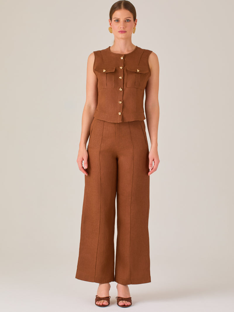 Este pantalón presenta un corte de pierna ancha y recta, confeccionado en una tela estructurada de tono marrón cálido. Tiene un diseño elegante y minimalista, con cintura de talle medio y cierre delantero oculto. Las líneas limpias y la ausencia de detalles recargados lo hacen ideal para un look pulido y sofisticado. Incluye bolsillos discretos laterales y se ajusta ligeramente en la cadera, cayendo con amplitud hasta los tobillos. Su estilo versátil lo convierte en una prenda perfecta tanto para contextos 