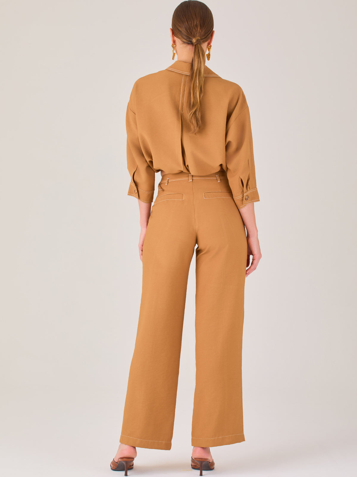 Este pantalón tiene un diseño sofisticado y moderno, confeccionado en un tono beige claro muy versátil. Presenta una silueta de pierna recta y ligeramente amplia, lo que aporta una caída elegante y cómoda. La cintura es de talle medio-alto, con cierre delantero oculto y detalles de pinzas que estilizan la figura. Incluye trabillas para cinturón y bolsillos laterales funcionales, además de costuras marcadas al frente que aportan estructura. Es una prenda ideal para looks de oficina, conjuntos monocromáticos 