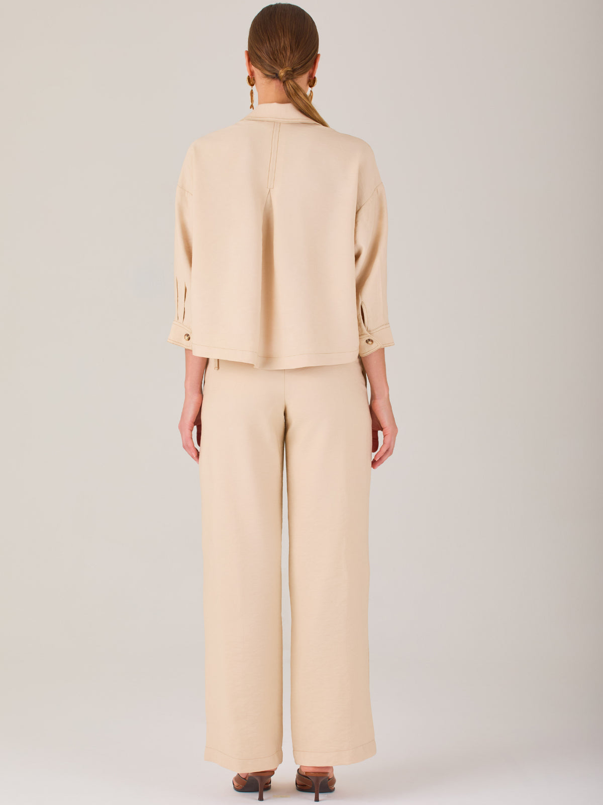 Este pantalón tiene un diseño sofisticado y moderno, confeccionado en un tono beige claro muy versátil. Presenta una silueta de pierna recta y ligeramente amplia, lo que aporta una caída elegante y cómoda. La cintura es de talle medio-alto, con cierre delantero oculto y detalles de pinzas que estilizan la figura. Incluye trabillas para cinturón y bolsillos laterales funcionales, además de costuras marcadas al frente que aportan estructura. Es una prenda ideal para looks de oficina, conjuntos monocromáticos 