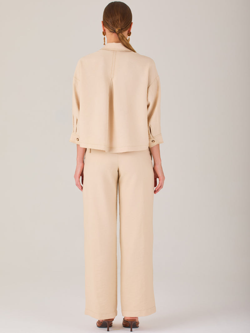 Este pantalón tiene un diseño sofisticado y moderno, confeccionado en un tono beige claro muy versátil. Presenta una silueta de pierna recta y ligeramente amplia, lo que aporta una caída elegante y cómoda. La cintura es de talle medio-alto, con cierre delantero oculto y detalles de pinzas que estilizan la figura. Incluye trabillas para cinturón y bolsillos laterales funcionales, además de costuras marcadas al frente que aportan estructura. Es una prenda ideal para looks de oficina, conjuntos monocromáticos 