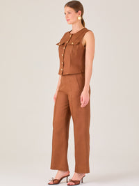 Este pantalón presenta un corte de pierna ancha y recta, confeccionado en una tela estructurada de tono marrón cálido. Tiene un diseño elegante y minimalista, con cintura de talle medio y cierre delantero oculto. Las líneas limpias y la ausencia de detalles recargados lo hacen ideal para un look pulido y sofisticado. Incluye bolsillos discretos laterales y se ajusta ligeramente en la cadera, cayendo con amplitud hasta los tobillos. Su estilo versátil lo convierte en una prenda perfecta tanto para contextos 
