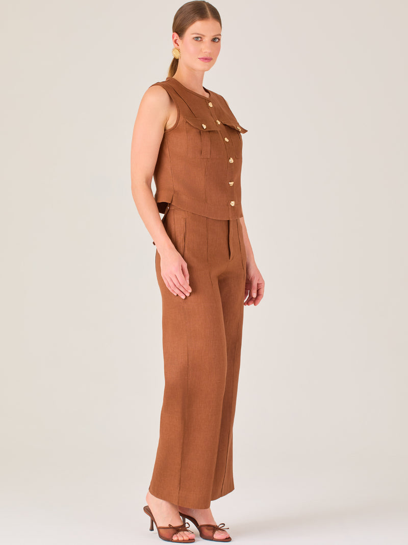 Este pantalón presenta un corte de pierna ancha y recta, confeccionado en una tela estructurada de tono marrón cálido. Tiene un diseño elegante y minimalista, con cintura de talle medio y cierre delantero oculto. Las líneas limpias y la ausencia de detalles recargados lo hacen ideal para un look pulido y sofisticado. Incluye bolsillos discretos laterales y se ajusta ligeramente en la cadera, cayendo con amplitud hasta los tobillos. Su estilo versátil lo convierte en una prenda perfecta tanto para contextos 
