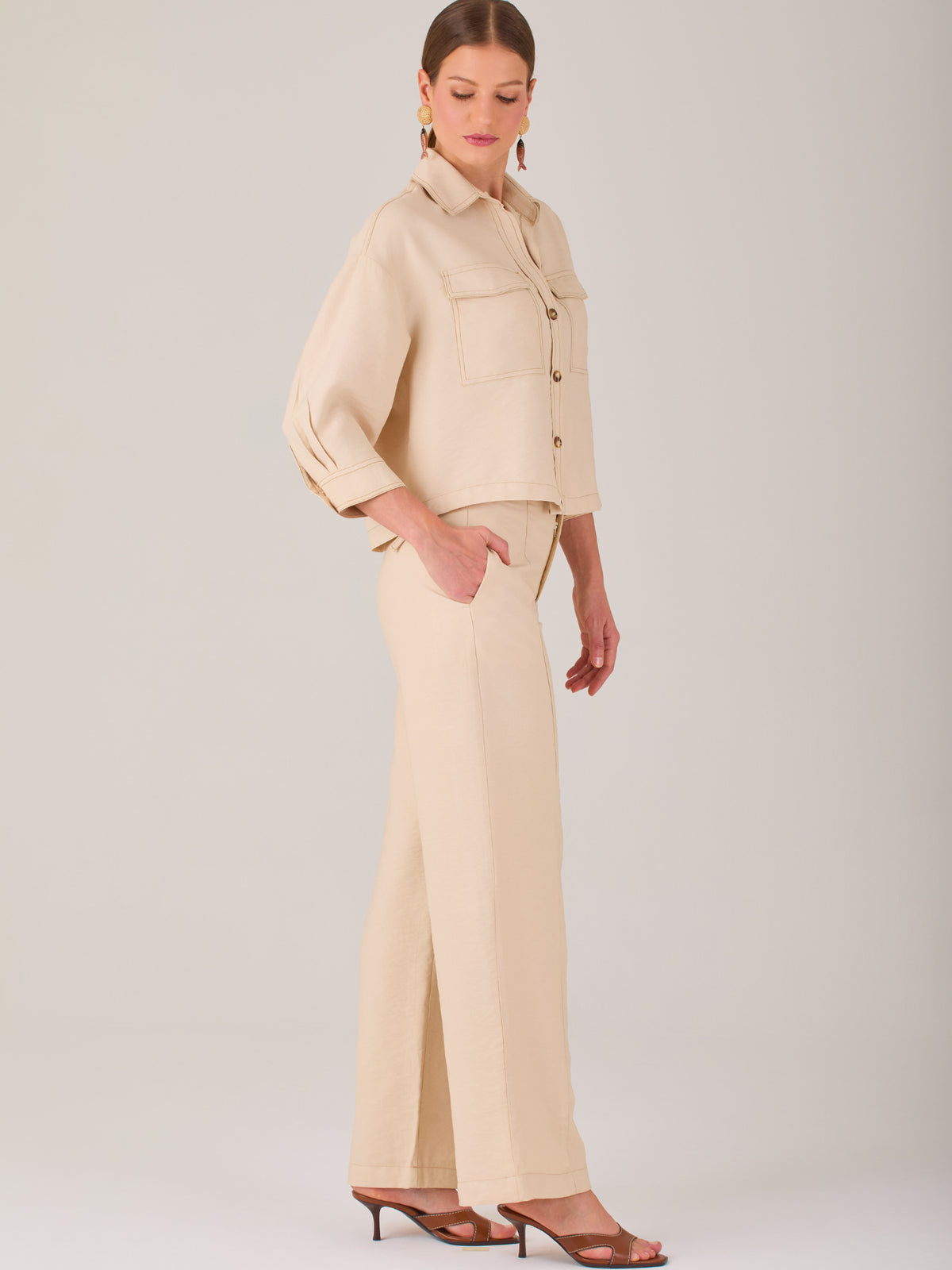Este pantalón tiene un diseño sofisticado y moderno, confeccionado en un tono beige claro muy versátil. Presenta una silueta de pierna recta y ligeramente amplia, lo que aporta una caída elegante y cómoda. La cintura es de talle medio-alto, con cierre delantero oculto y detalles de pinzas que estilizan la figura. Incluye trabillas para cinturón y bolsillos laterales funcionales, además de costuras marcadas al frente que aportan estructura. Es una prenda ideal para looks de oficina, conjuntos monocromáticos 
