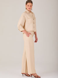 Este pantalón tiene un diseño sofisticado y moderno, confeccionado en un tono beige claro muy versátil. Presenta una silueta de pierna recta y ligeramente amplia, lo que aporta una caída elegante y cómoda. La cintura es de talle medio-alto, con cierre delantero oculto y detalles de pinzas que estilizan la figura. Incluye trabillas para cinturón y bolsillos laterales funcionales, además de costuras marcadas al frente que aportan estructura. Es una prenda ideal para looks de oficina, conjuntos monocromáticos 
