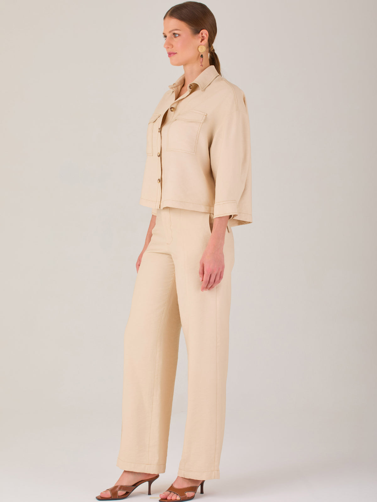 Este pantalón tiene un diseño sofisticado y moderno, confeccionado en un tono beige claro muy versátil. Presenta una silueta de pierna recta y ligeramente amplia, lo que aporta una caída elegante y cómoda. La cintura es de talle medio-alto, con cierre delantero oculto y detalles de pinzas que estilizan la figura. Incluye trabillas para cinturón y bolsillos laterales funcionales, además de costuras marcadas al frente que aportan estructura. Es una prenda ideal para looks de oficina, conjuntos monocromáticos 