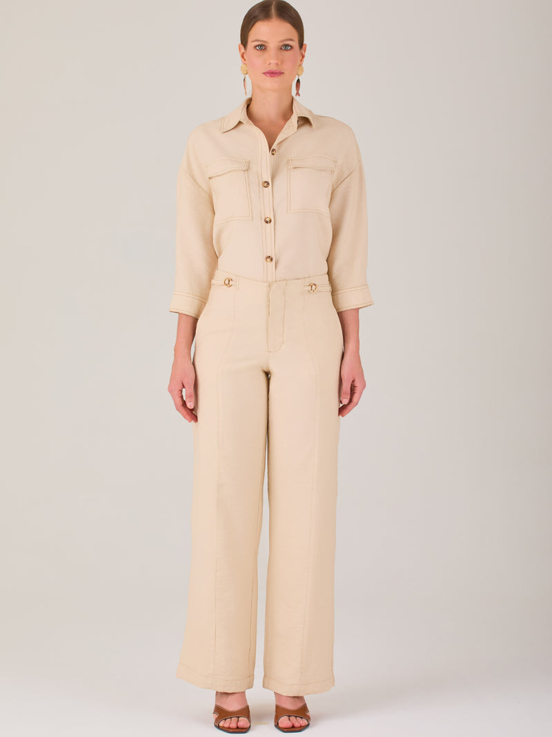Este pantalón tiene un diseño sofisticado y moderno, confeccionado en un tono beige claro muy versátil. Presenta una silueta de pierna recta y ligeramente amplia, lo que aporta una caída elegante y cómoda. La cintura es de talle medio-alto, con cierre delantero oculto y detalles de pinzas que estilizan la figura. Incluye trabillas para cinturón y bolsillos laterales funcionales, además de costuras marcadas al frente que aportan estructura. Es una prenda ideal para looks de oficina, conjuntos monocromáticos 
