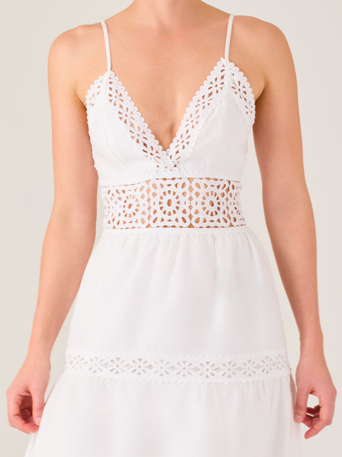 Este vestido largo blanco tiene un estilo fresco, romántico y veraniego. Cuenta con finos tirantes y un escote en “V” pronunciado, delicadamente adornado con bordado tipo encaje floral que continúa en la cintura, generando un efecto de transparencia sutil y elegante.

La falda de corte amplio y largo midi cae suavemente desde la cintura, con detalles de franjas horizontales de bordado calado que repiten el motivo floral. El tejido ligero y vaporoso aporta comodidad y libertad de movimiento.