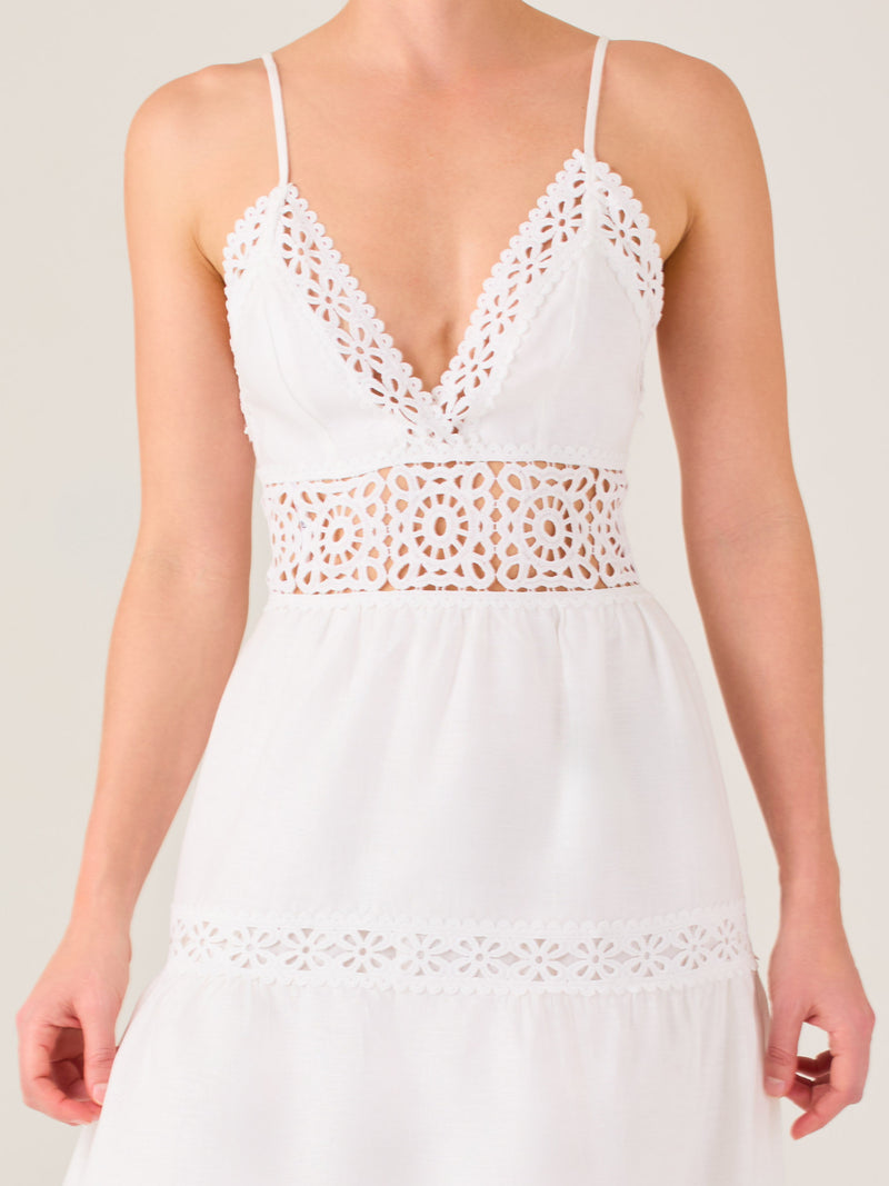 Este vestido largo blanco tiene un estilo fresco, romántico y veraniego. Cuenta con finos tirantes y un escote en “V” pronunciado, delicadamente adornado con bordado tipo encaje floral que continúa en la cintura, generando un efecto de transparencia sutil y elegante.

La falda de corte amplio y largo midi cae suavemente desde la cintura, con detalles de franjas horizontales de bordado calado que repiten el motivo floral. El tejido ligero y vaporoso aporta comodidad y libertad de movimiento.