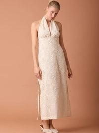 Vestido largo beige con escote halter profundo y textura decorativa perfecto para eventos y fiestas.