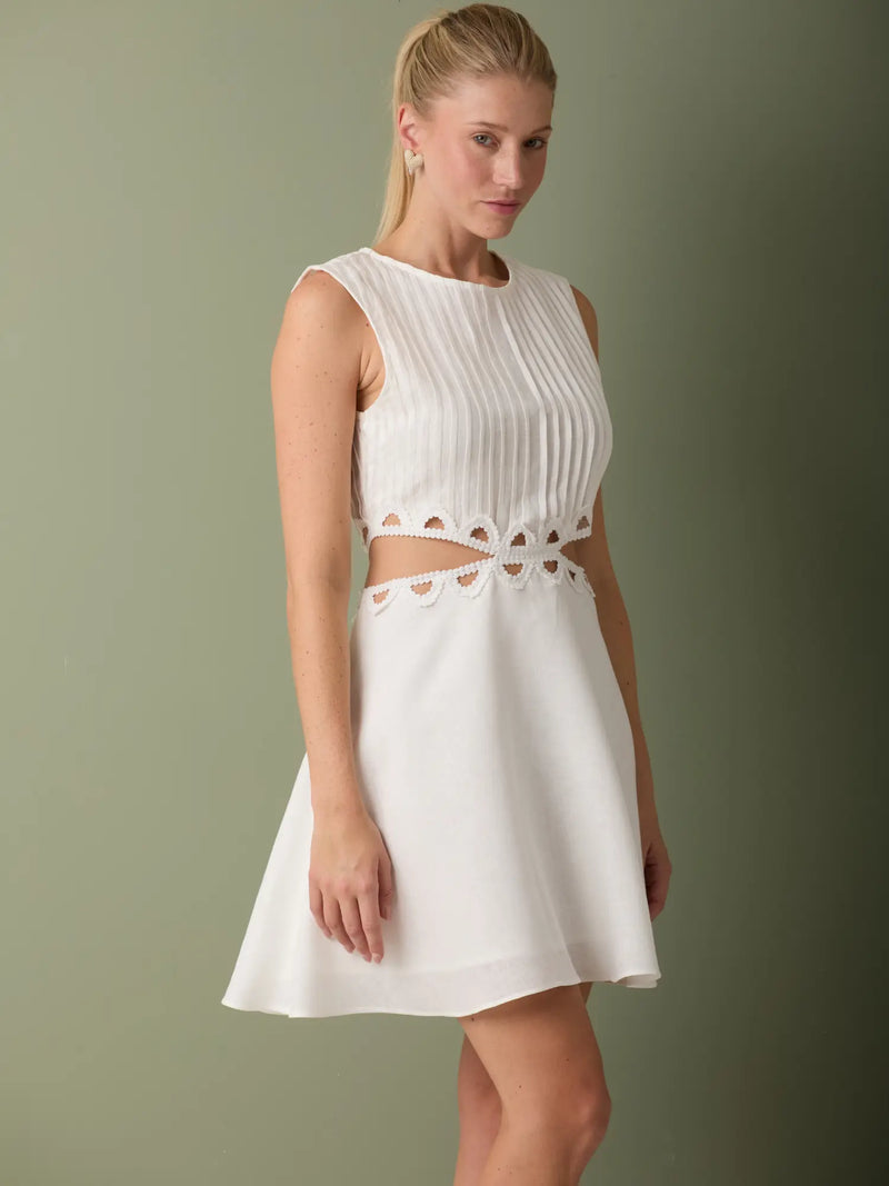 Vestido blanco corto delicado con recortes decorativos y falda suave con movimiento natural.