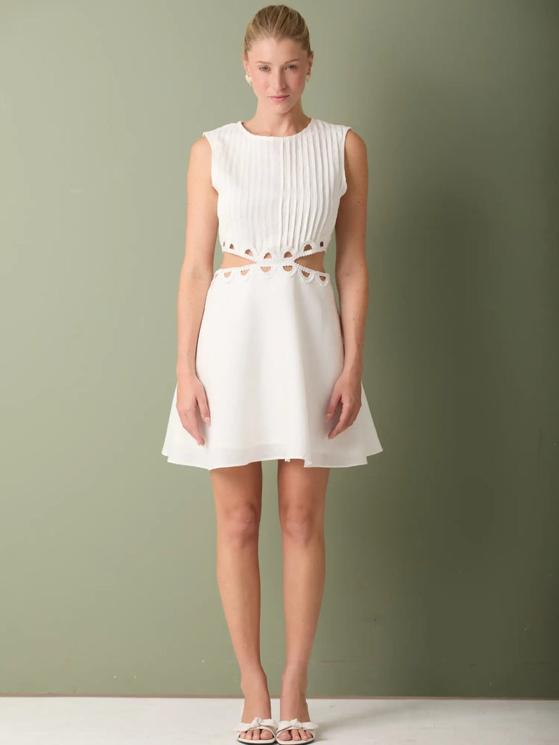 Vestido blanco corto elegante con detalle plisado y recortes laterales que estilizan la figura.