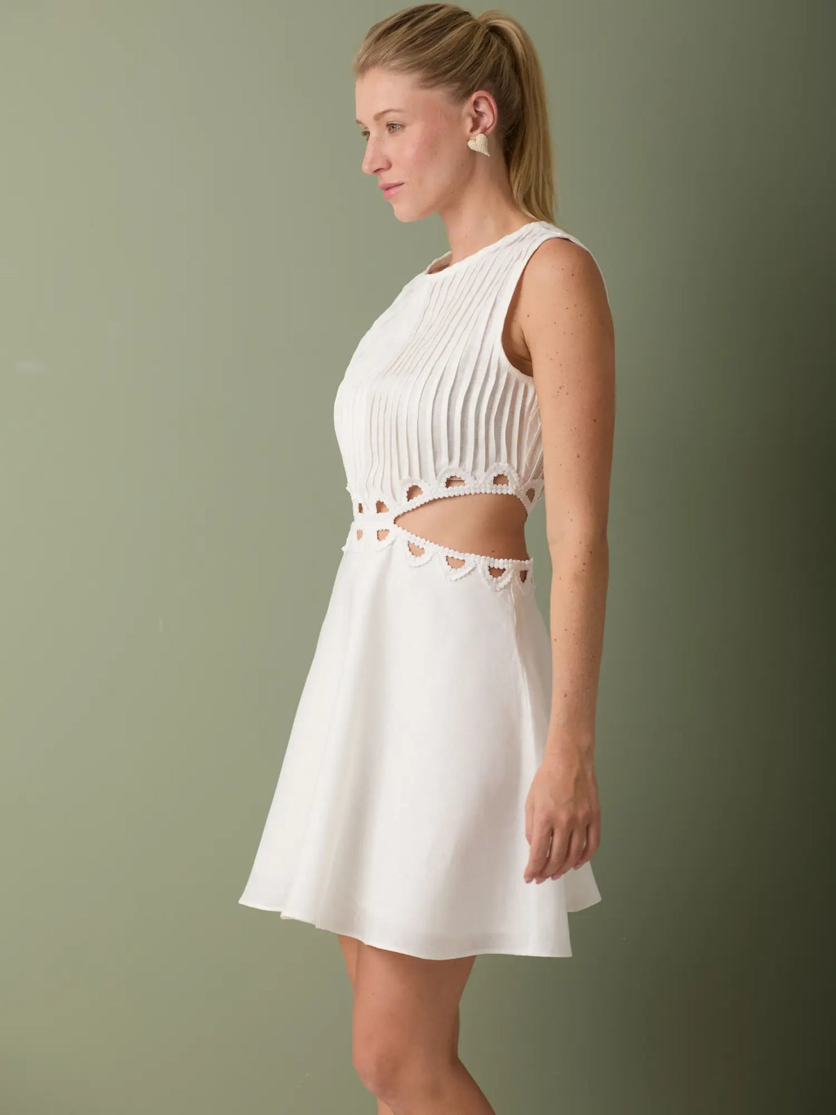 Vestido blanco formal corto con cuerpo plisado y aberturas decorativas que aportan frescura.