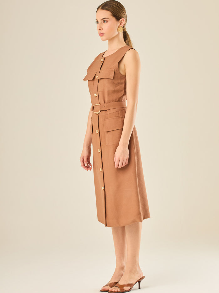 Vestido sin mangas con botonadura frontal y cinturón a tono con hebilla dorada. Tiene bolsillos tipo parche en el pecho y la cadera que acentúan su aire utilitario, mientras que el largo midi y los botones metálicos le dan un acabado elegante y atemporal. Perfecto para un look sofisticado de día.