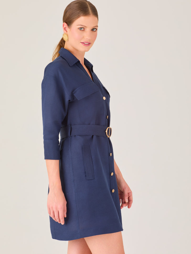 Vestido tipo camisero corto, con cuello clásico, mangas tres cuartos, botones frontales y cinturón con hebilla dorada. Estilo elegante y casual.