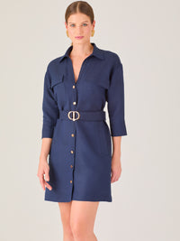 Vestido tipo camisero corto, con cuello clásico, mangas tres cuartos, botones frontales y cinturón con hebilla dorada. Estilo elegante y casual.