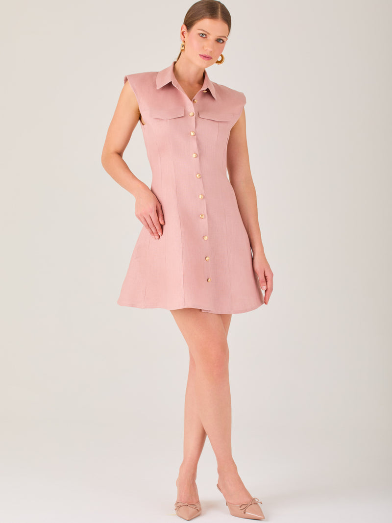 Este vestido sin mangas tiene un diseño camisero de corte recto con estructura entallada en la parte superior que se ajusta a la silueta. Tiene cuello tipo camisa y una botonadura completa al frente con botones grandes y visibles. A la altura del pecho, incluye dos bolsillos de parche con solapa, añadiendo un detalle funcional y decorativo. La falda tiene una caída en línea A, que da un toque femenino y ligeramente acampanado. La parte trasera mantiene la sencillez con costuras que definen la forma del vest