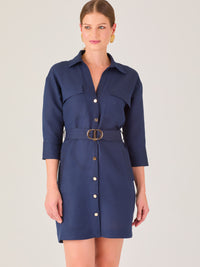 Vestido tipo camisero corto, con cuello clásico, mangas tres cuartos, botones frontales y cinturón con hebilla dorada. Estilo elegante y casual.