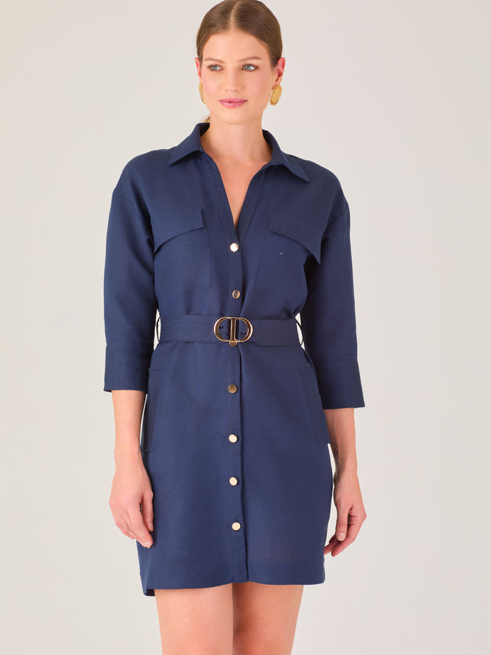 Vestido tipo camisero corto, con cuello clásico, mangas tres cuartos, botones frontales y cinturón con hebilla dorada. Estilo elegante y casual.