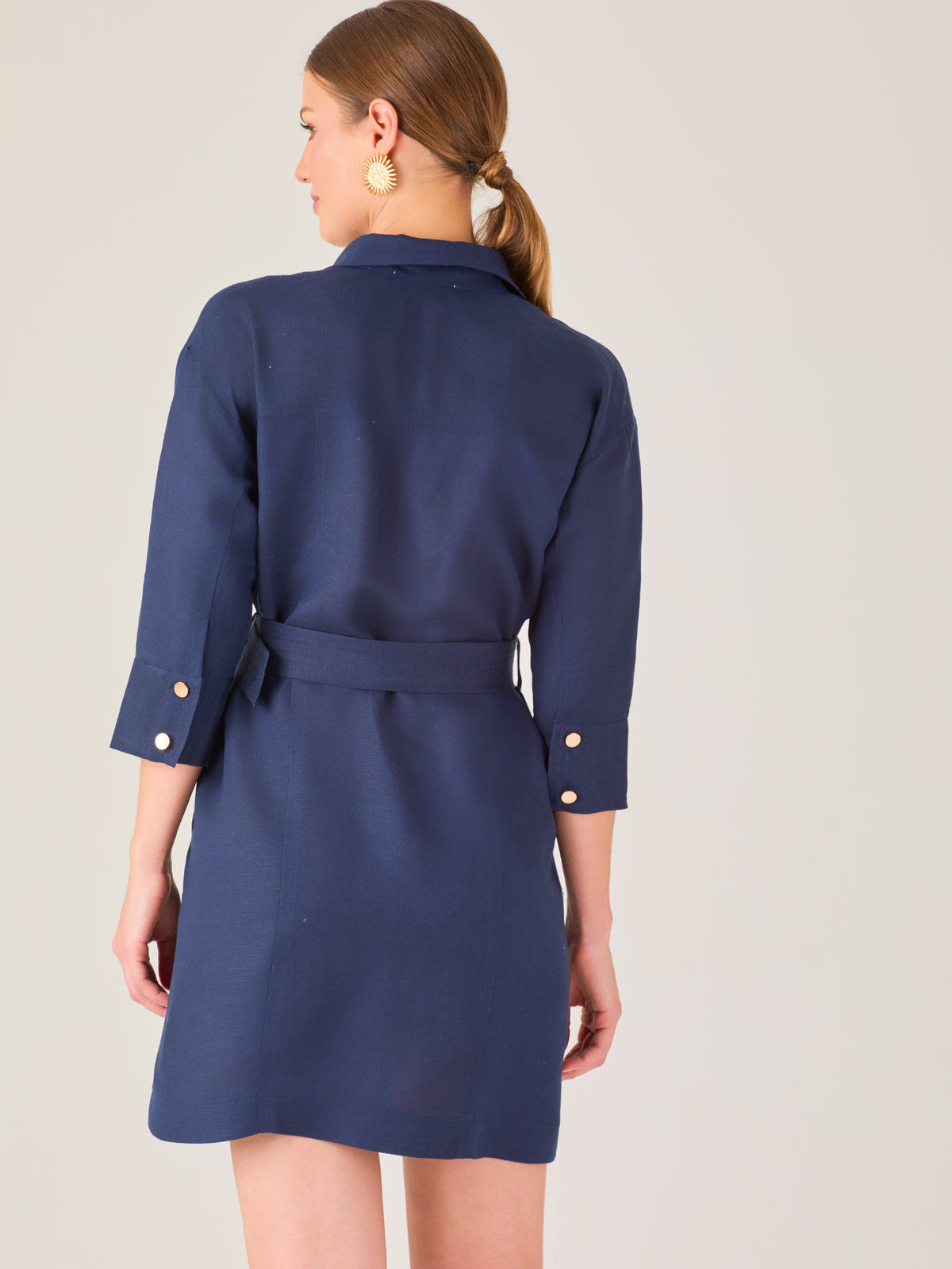 Vestido tipo camisero corto, con cuello clásico, mangas tres cuartos, botones frontales y cinturón con hebilla dorada. Estilo elegante y casual.