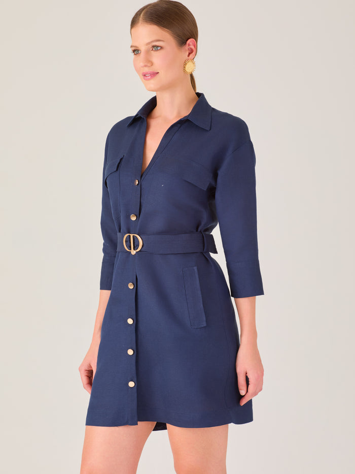 Vestido tipo camisero corto, con cuello clásico, mangas tres cuartos, botones frontales y cinturón con hebilla dorada. Estilo elegante y casual.