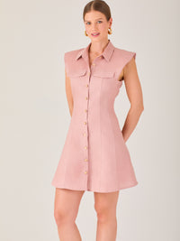 Este vestido sin mangas tiene un diseño camisero de corte recto con estructura entallada en la parte superior que se ajusta a la silueta. Tiene cuello tipo camisa y una botonadura completa al frente con botones grandes y visibles. A la altura del pecho, incluye dos bolsillos de parche con solapa, añadiendo un detalle funcional y decorativo. La falda tiene una caída en línea A, que da un toque femenino y ligeramente acampanado. La parte trasera mantiene la sencillez con costuras que definen la forma del vest