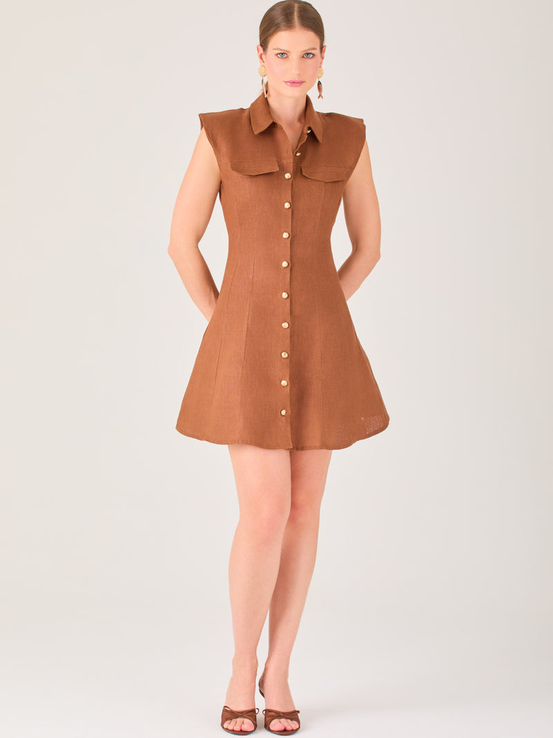 Este vestido sin mangas tiene un diseño camisero de corte recto con estructura entallada en la parte superior que se ajusta a la silueta. Tiene cuello tipo camisa y una botonadura completa al frente con botones grandes y visibles. A la altura del pecho, incluye dos bolsillos de parche con solapa, añadiendo un detalle funcional y decorativo. La falda tiene una caída en línea A, que da un toque femenino y ligeramente acampanado. La parte trasera mantiene la sencillez con costuras que definen la forma del vest