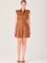 Este vestido sin mangas tiene un diseño camisero de corte recto con estructura entallada en la parte superior que se ajusta a la silueta. Tiene cuello tipo camisa y una botonadura completa al frente con botones grandes y visibles. A la altura del pecho, incluye dos bolsillos de parche con solapa, añadiendo un detalle funcional y decorativo. La falda tiene una caída en línea A, que da un toque femenino y ligeramente acampanado. La parte trasera mantiene la sencillez con costuras que definen la forma del vest