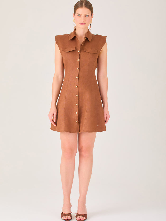 Este vestido sin mangas tiene un diseño camisero de corte recto con estructura entallada en la parte superior que se ajusta a la silueta. Tiene cuello tipo camisa y una botonadura completa al frente con botones grandes y visibles. A la altura del pecho, incluye dos bolsillos de parche con solapa, añadiendo un detalle funcional y decorativo. La falda tiene una caída en línea A, que da un toque femenino y ligeramente acampanado. La parte trasera mantiene la sencillez con costuras que definen la forma del vest