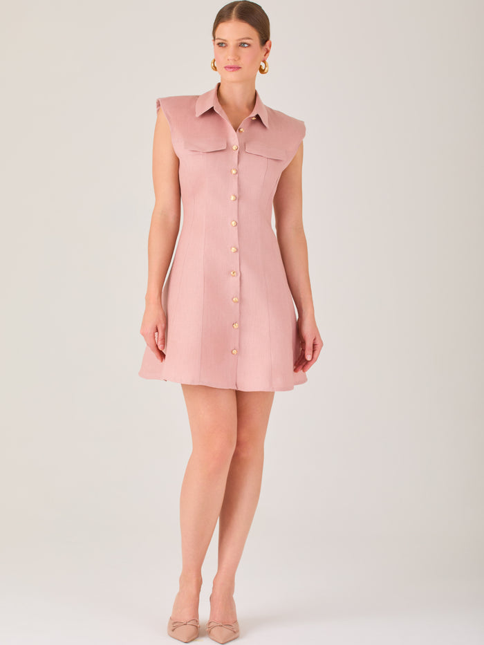 Este vestido sin mangas tiene un diseño camisero de corte recto con estructura entallada en la parte superior que se ajusta a la silueta. Tiene cuello tipo camisa y una botonadura completa al frente con botones grandes y visibles. A la altura del pecho, incluye dos bolsillos de parche con solapa, añadiendo un detalle funcional y decorativo. La falda tiene una caída en línea A, que da un toque femenino y ligeramente acampanado. La parte trasera mantiene la sencillez con costuras que definen la forma del vest