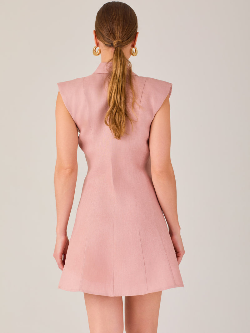 Este vestido sin mangas tiene un diseño camisero de corte recto con estructura entallada en la parte superior que se ajusta a la silueta. Tiene cuello tipo camisa y una botonadura completa al frente con botones grandes y visibles. A la altura del pecho, incluye dos bolsillos de parche con solapa, añadiendo un detalle funcional y decorativo. La falda tiene una caída en línea A, que da un toque femenino y ligeramente acampanado. La parte trasera mantiene la sencillez con costuras que definen la forma del vest