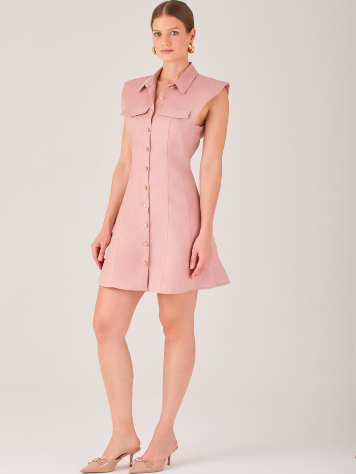 Este vestido sin mangas tiene un diseño camisero de corte recto con estructura entallada en la parte superior que se ajusta a la silueta. Tiene cuello tipo camisa y una botonadura completa al frente con botones grandes y visibles. A la altura del pecho, incluye dos bolsillos de parche con solapa, añadiendo un detalle funcional y decorativo. La falda tiene una caída en línea A, que da un toque femenino y ligeramente acampanado. La parte trasera mantiene la sencillez con costuras que definen la forma del vest