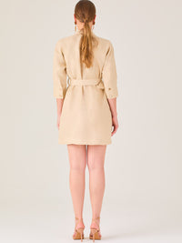 Vestido tipo camisero beige, corto, con cuello clásico, mangas tres cuartos, botones frontales y cinturón con hebilla dorada. Estilo elegante y casual.