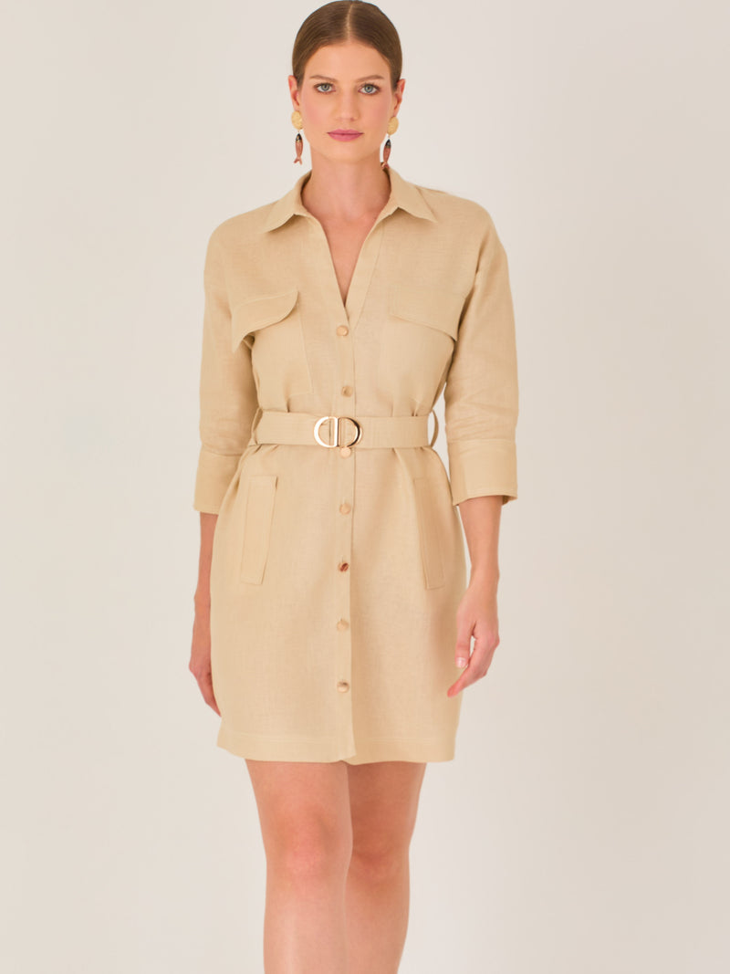 Vestido tipo camisero beige, corto, con cuello clásico, mangas tres cuartos, botones frontales y cinturón con hebilla dorada. Estilo elegante y casual.