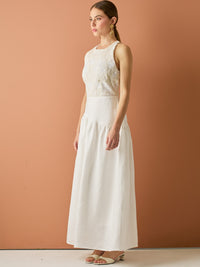Vestido largo sin mangas con escote halter y cuerpo bordado en delicado encaje. La falda de lino con caída fluida aporta frescura y movimiento, creando una silueta femenina y elegante ideal para ocasiones especiales con un aire natural y sofisticado.