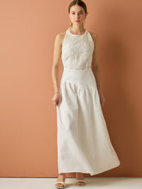 Vestido largo sin mangas con escote halter y cuerpo bordado en delicado encaje. La falda de lino con caída fluida aporta frescura y movimiento, creando una silueta femenina y elegante ideal para ocasiones especiales con un aire natural y sofisticado.