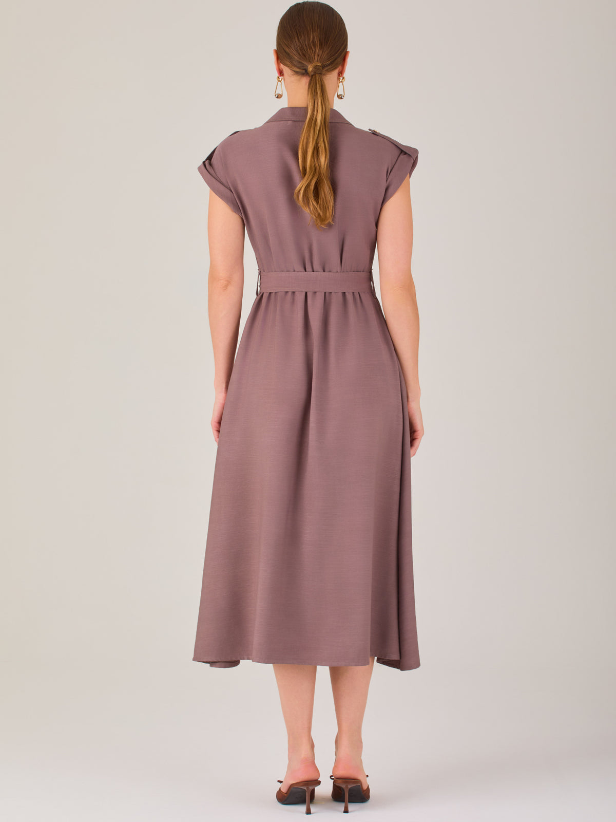 Diseño atemporal con carácter. Este vestido midi sin mangas combina estructura y feminidad con detalles utilitarios como bolsillos frontales, cierre metálico y solapas marcadas. El cinturón en la cintura permite ajustar la silueta, creando un look pulido ideal para la oficina, eventos casuales o estilismos urbanos con elegancia natural.