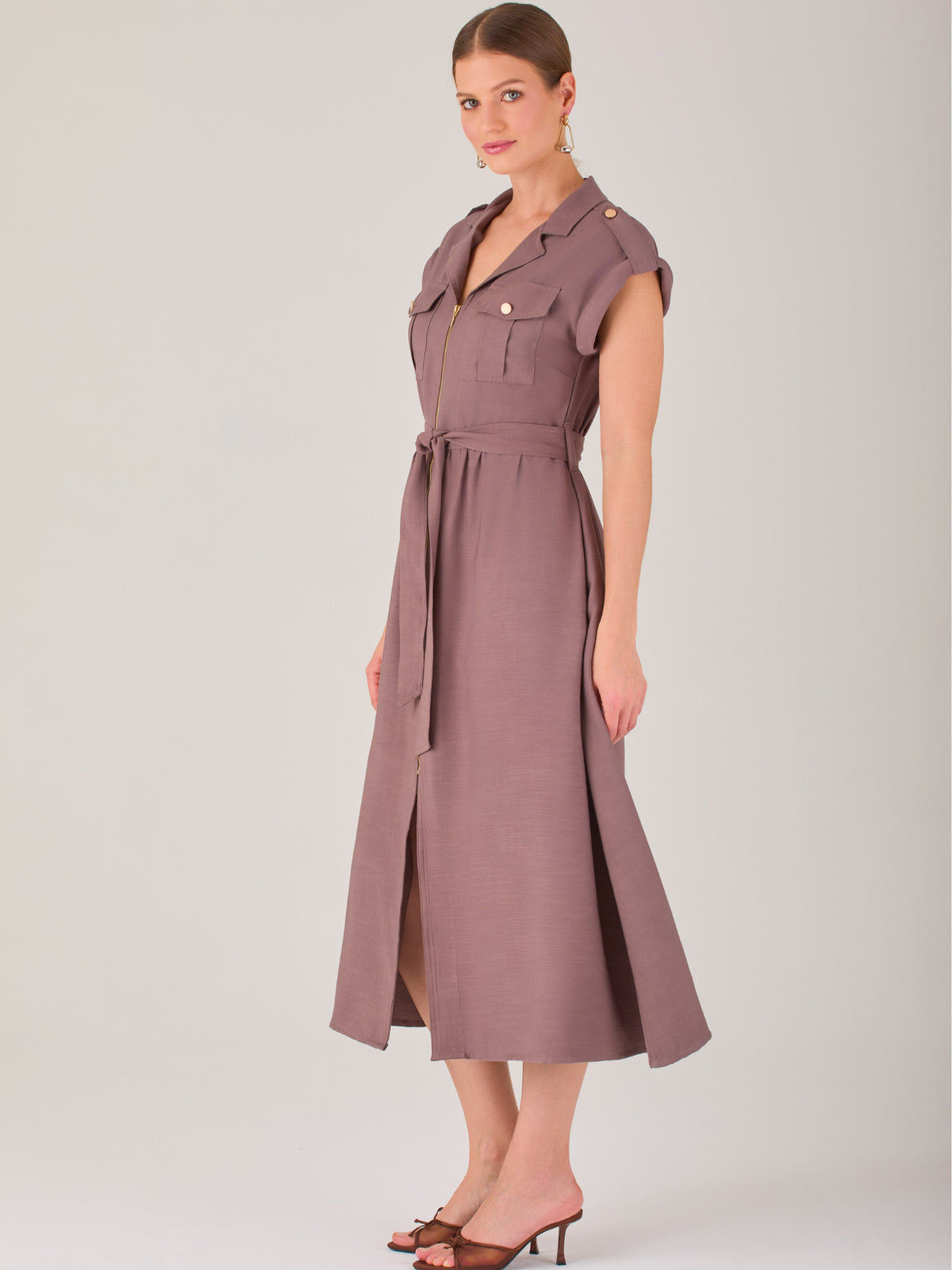 Diseño atemporal con carácter. Este vestido midi sin mangas combina estructura y feminidad con detalles utilitarios como bolsillos frontales, cierre metálico y solapas marcadas. El cinturón en la cintura permite ajustar la silueta, creando un look pulido ideal para la oficina, eventos casuales o estilismos urbanos con elegancia natural.