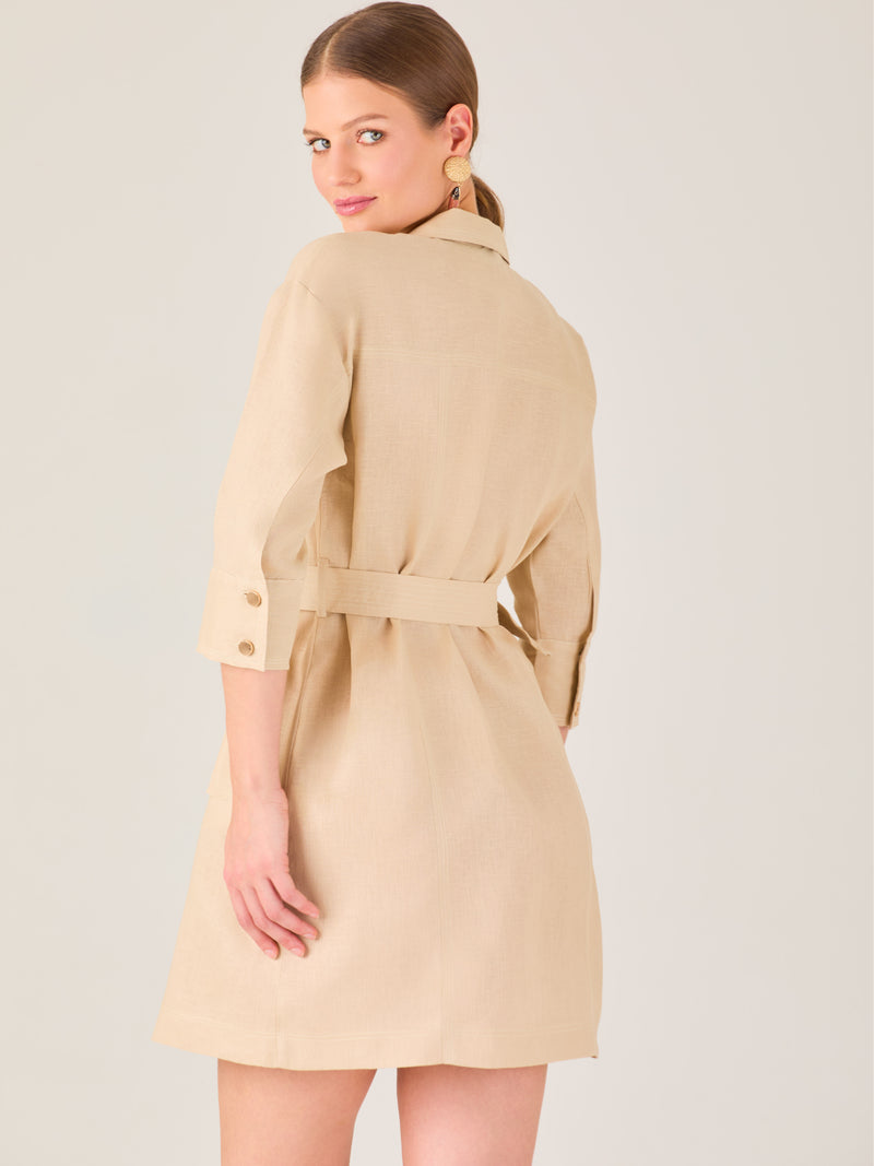 Vestido tipo camisero beige, corto, con cuello clásico, mangas tres cuartos, botones frontales y cinturón con hebilla dorada. Estilo elegante y casual.