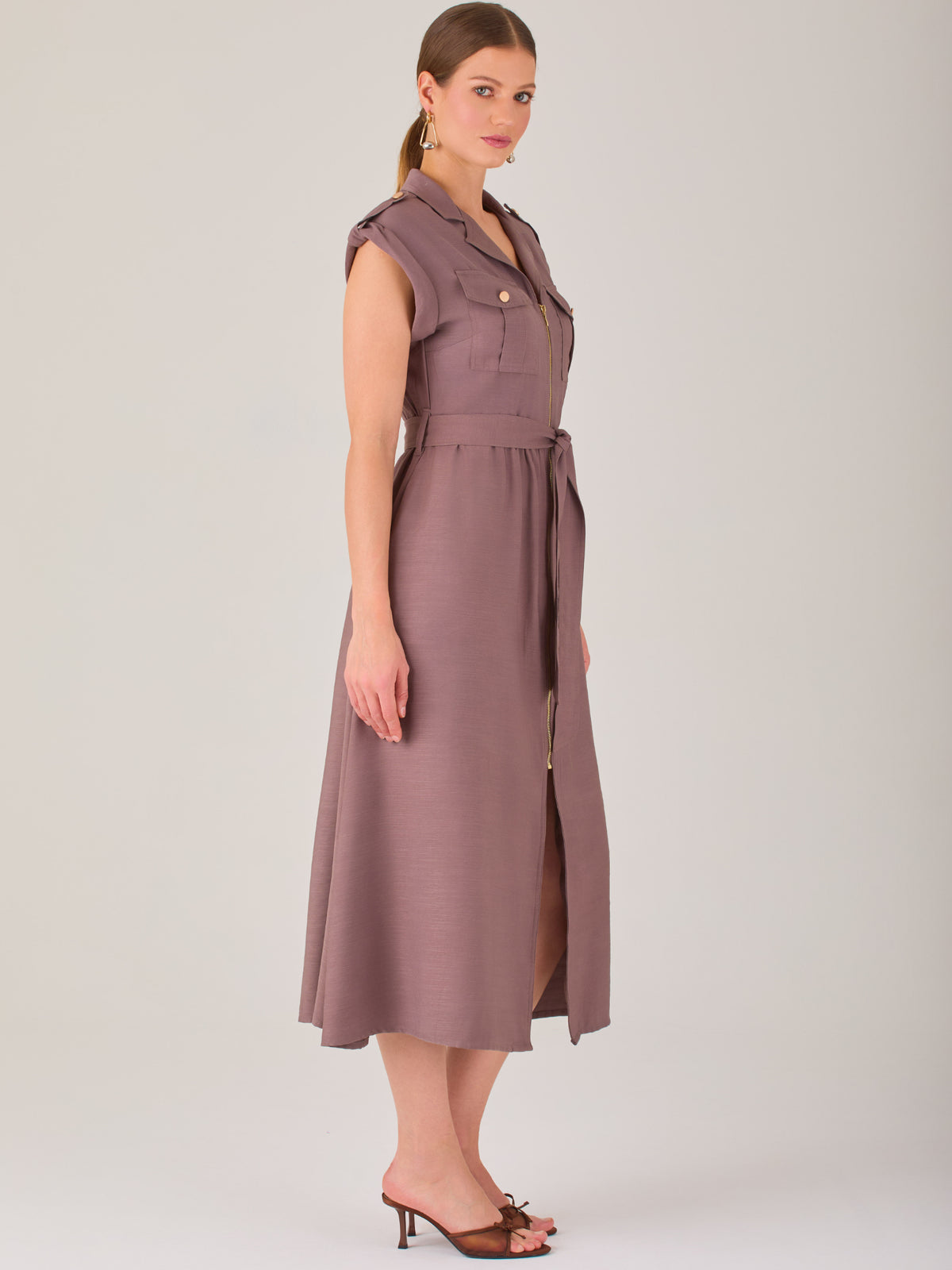 Diseño atemporal con carácter. Este vestido midi sin mangas combina estructura y feminidad con detalles utilitarios como bolsillos frontales, cierre metálico y solapas marcadas. El cinturón en la cintura permite ajustar la silueta, creando un look pulido ideal para la oficina, eventos casuales o estilismos urbanos con elegancia natural.