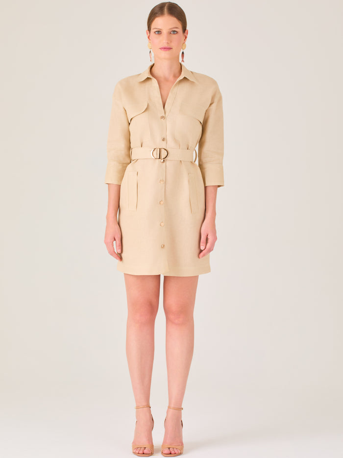Vestido tipo camisero beige, corto, con cuello clásico, mangas tres cuartos, botones frontales y cinturón con hebilla dorada. Estilo elegante y casual.