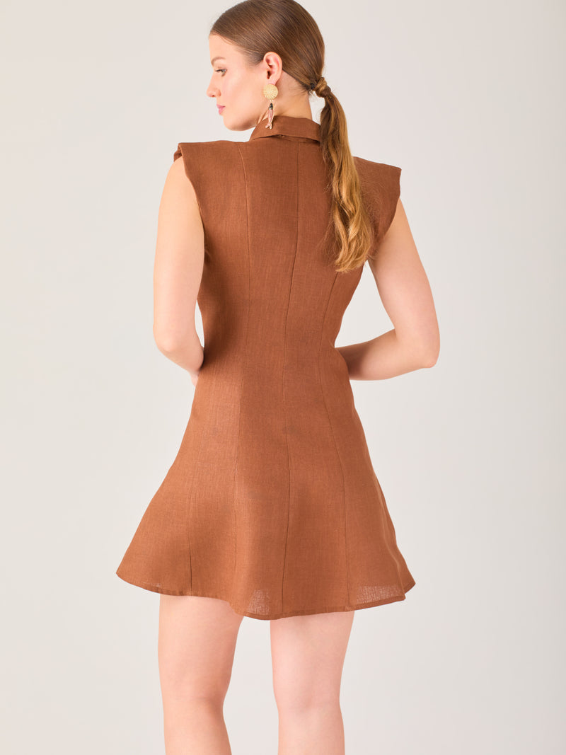 Este vestido sin mangas tiene un diseño camisero de corte recto con estructura entallada en la parte superior que se ajusta a la silueta. Tiene cuello tipo camisa y una botonadura completa al frente con botones grandes y visibles. A la altura del pecho, incluye dos bolsillos de parche con solapa, añadiendo un detalle funcional y decorativo. La falda tiene una caída en línea A, que da un toque femenino y ligeramente acampanado. La parte trasera mantiene la sencillez con costuras que definen la forma del vest