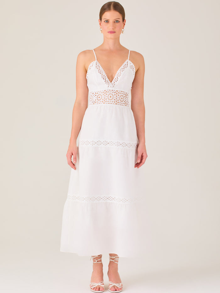 Este vestido largo blanco tiene un estilo fresco, romántico y veraniego. Cuenta con finos tirantes y un escote en “V” pronunciado, delicadamente adornado con bordado tipo encaje floral que continúa en la cintura, generando un efecto de transparencia sutil y elegante.

La falda de corte amplio y largo midi cae suavemente desde la cintura, con detalles de franjas horizontales de bordado calado que repiten el motivo floral. El tejido ligero y vaporoso aporta comodidad y libertad de movimiento.