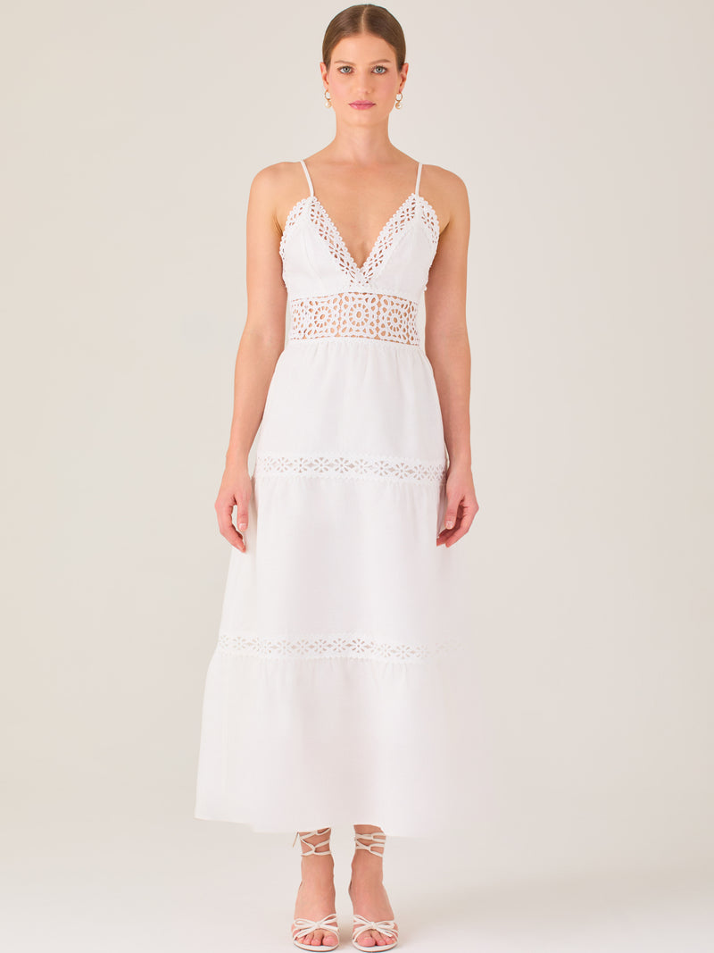 Este vestido largo blanco tiene un estilo fresco, romántico y veraniego. Cuenta con finos tirantes y un escote en “V” pronunciado, delicadamente adornado con bordado tipo encaje floral que continúa en la cintura, generando un efecto de transparencia sutil y elegante.

La falda de corte amplio y largo midi cae suavemente desde la cintura, con detalles de franjas horizontales de bordado calado que repiten el motivo floral. El tejido ligero y vaporoso aporta comodidad y libertad de movimiento.
