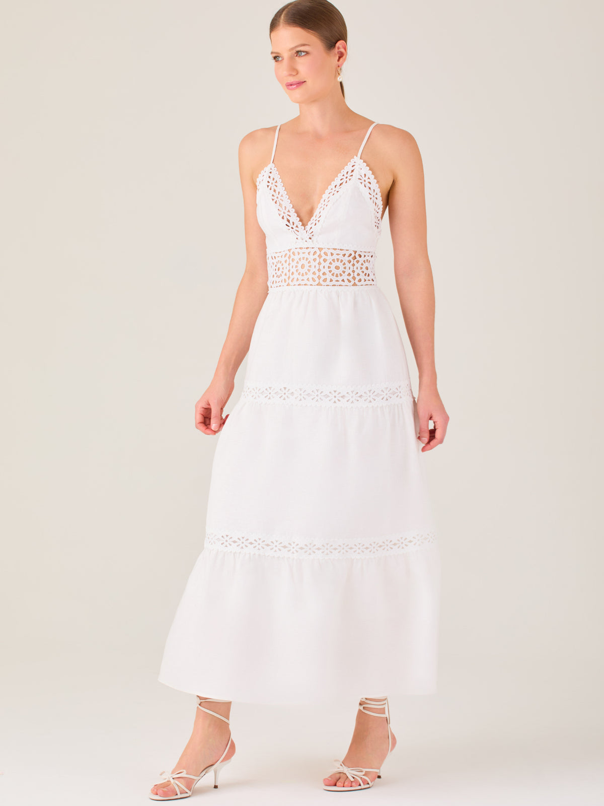 Este vestido largo blanco tiene un estilo fresco, romántico y veraniego. Cuenta con finos tirantes y un escote en “V” pronunciado, delicadamente adornado con bordado tipo encaje floral que continúa en la cintura, generando un efecto de transparencia sutil y elegante.

La falda de corte amplio y largo midi cae suavemente desde la cintura, con detalles de franjas horizontales de bordado calado que repiten el motivo floral. El tejido ligero y vaporoso aporta comodidad y libertad de movimiento.
